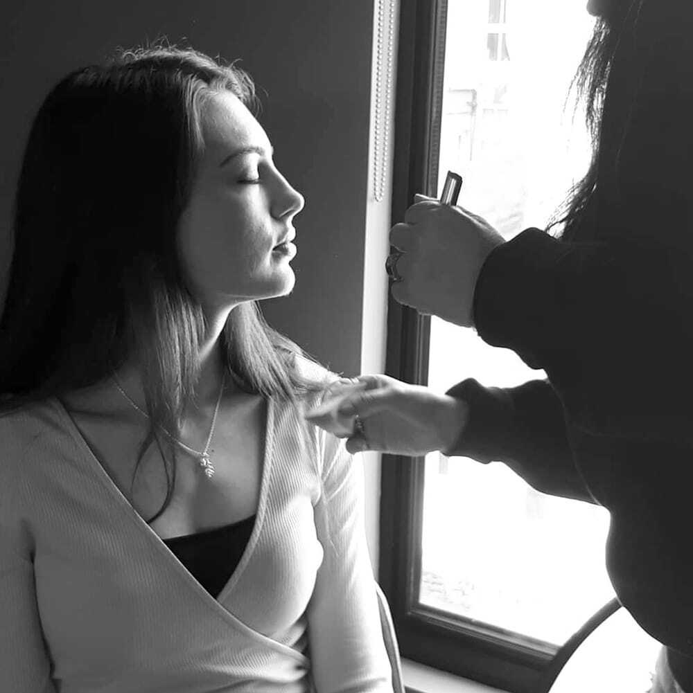 Behind the scenes of our photoshoots, brunette model sitting down with eyes closed getting makeup done in black and white