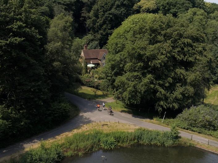Drone photography of cyclists in Sussex countryside near lake with cottage in background
